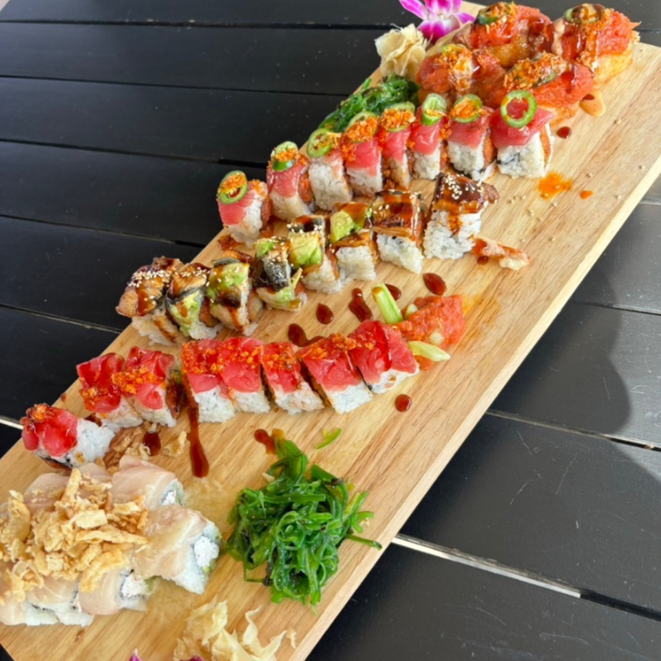 A large wooden board filled with various colorful sushi rolls, seaweed salad, and ginger.