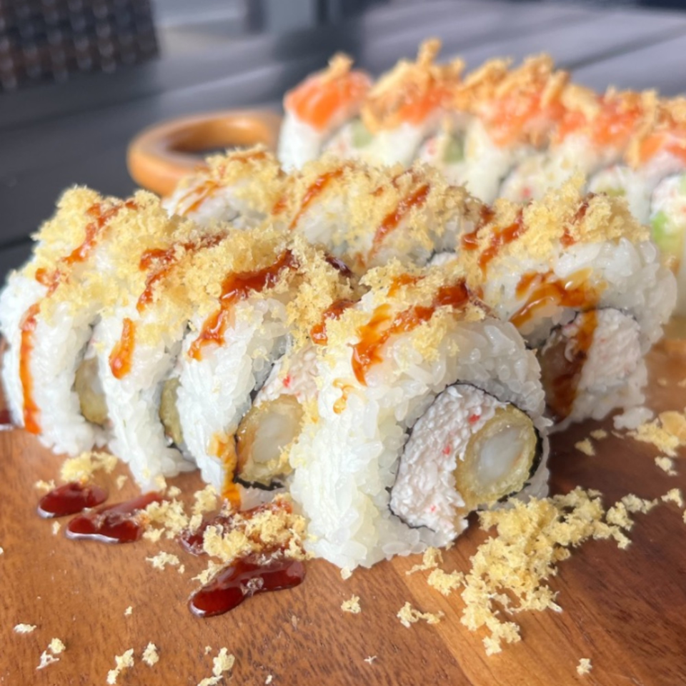 Hanamaru Sushi's crispy shrimp tempura rolls with sauce and salmon rolls on a wooden board.