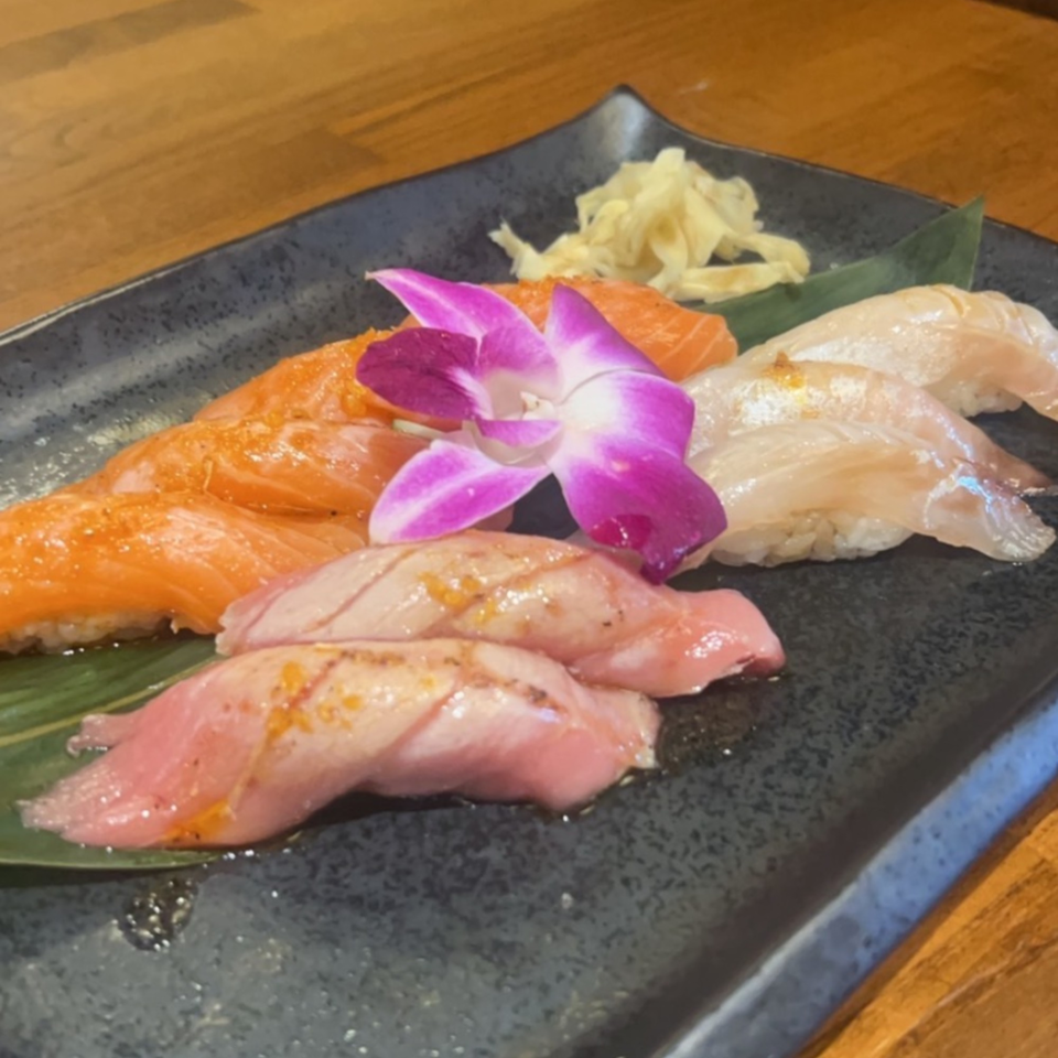 Hanamaru Sushi's nigiri platter with salmon, white fish, and seared tuna, garnished with a purple orchid.