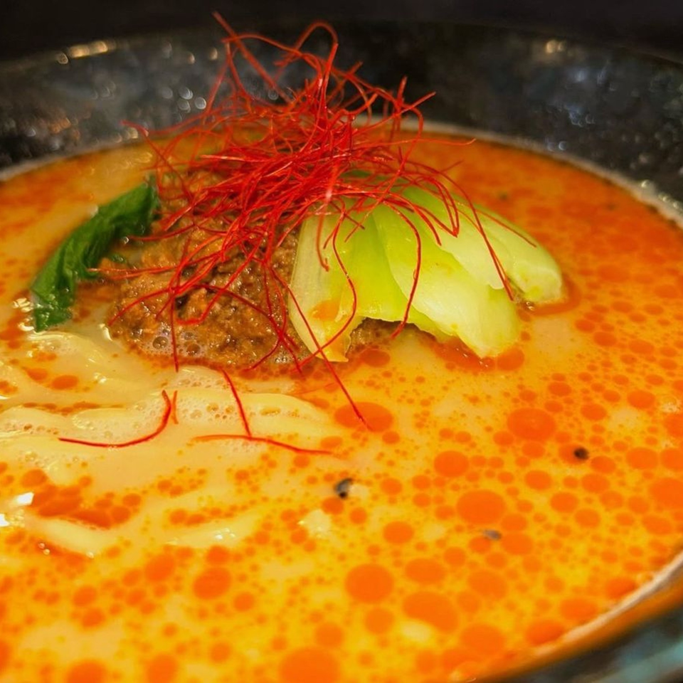 Spicy ramen with minced meat, bok choy, and red chili threads in a black bowl.