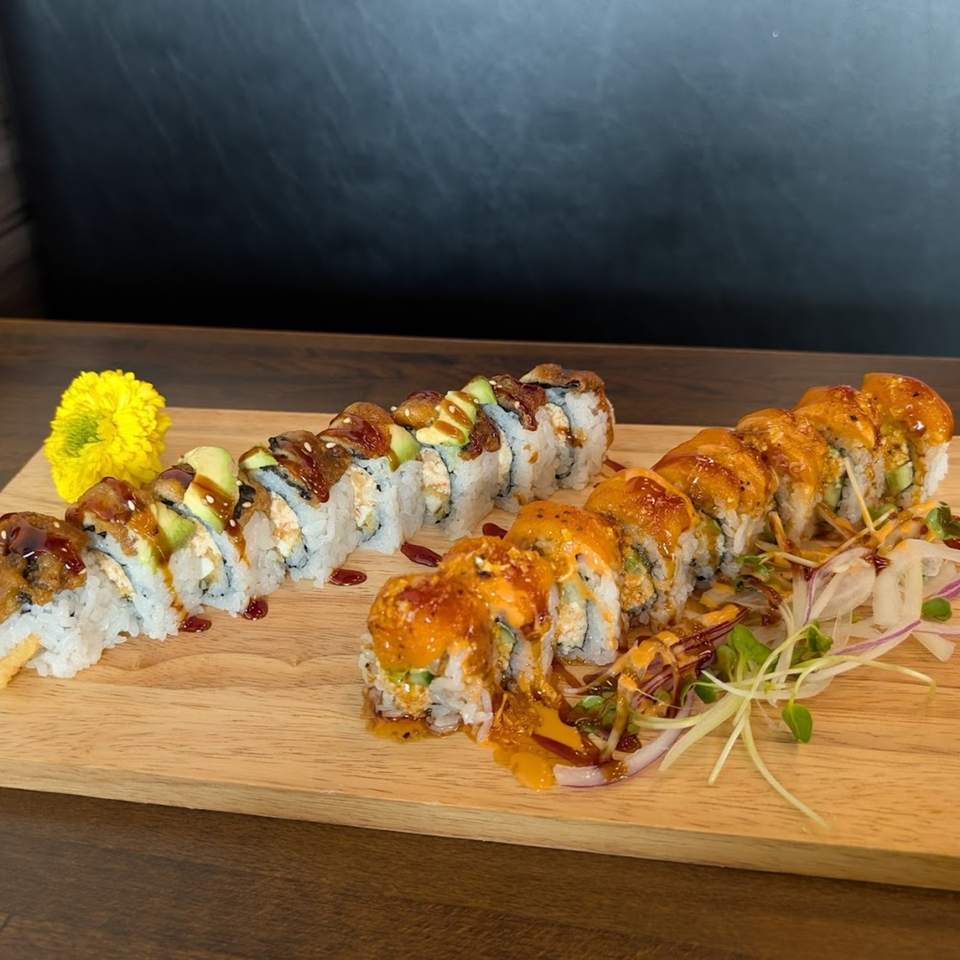 Two rows of Hanamaru Sushi rolls, one topped with eel and avocado, the other with spicy sauce.
